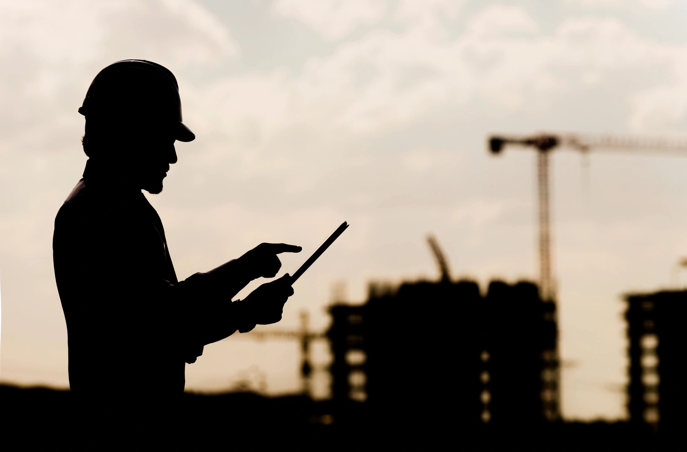Silhouette of a worker using a tablet at a construction site.